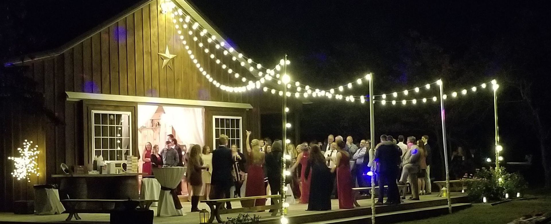 Wedding reception at night time. Bistro lights are strung from the barn to the deck.